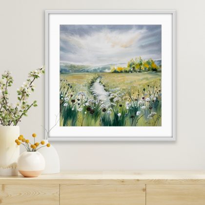 A watercolour painting of a narrow, silver stream winding through a wild meadow toward a distant treeline. Shown in a room above a sideboard. In the foreground, delicate white cow parsley and dark, silhouetted seed heads are painted with fine detail against a wash of green and gold grass.